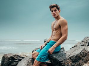海の岩場に座る筋肉質な男性